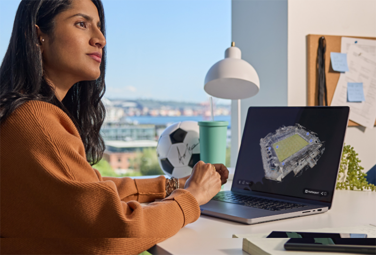 Woman sitting in front of a computer featuring a Matterport dollhouse view of a stadium